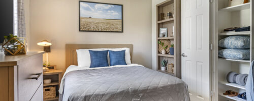 queen suite with bedside table, task lighting, and USB charging outlet. Bookcase on the wall to the right of the bed.