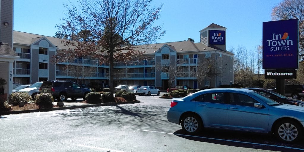 An InTown Suites property in Charleston with multiple cars parked in front and trees scattered around the parking lot.