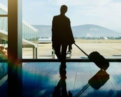 A man stands in airport, holding his luggage as he looks out over the tarmac.