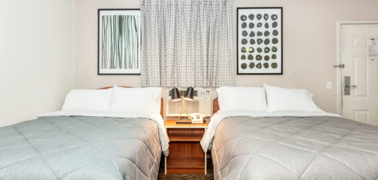Two beds with grey comforters and white pillows with two