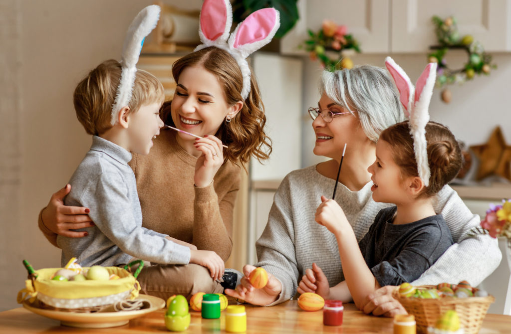 Mom, grandma and kids decorating Easter eggs at home, celebrating Easter safely.